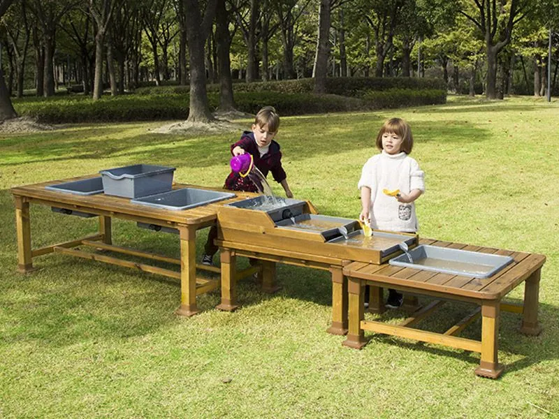Wasserbahn-Matschtisch-Set mit fröhlich spielenden Kindern auf dem Spielplatz Wasserbahn-Matschtisch-Set mit fröhlich spielenden Kindern auf dem Spielplatz