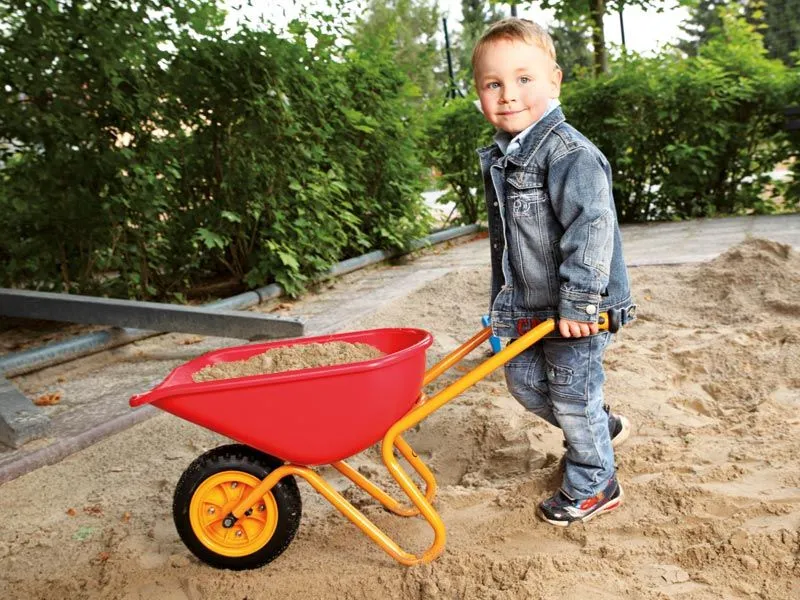 Kinderschubkarre gefüllt mit Sand und kleinem Jungen beim Transport
